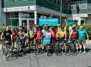 Group of cyclists standing in front of Cross Roads House shelter.