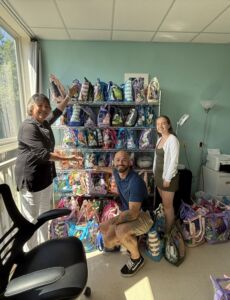 Cross Roads House staff stand next to summer fun bags.
